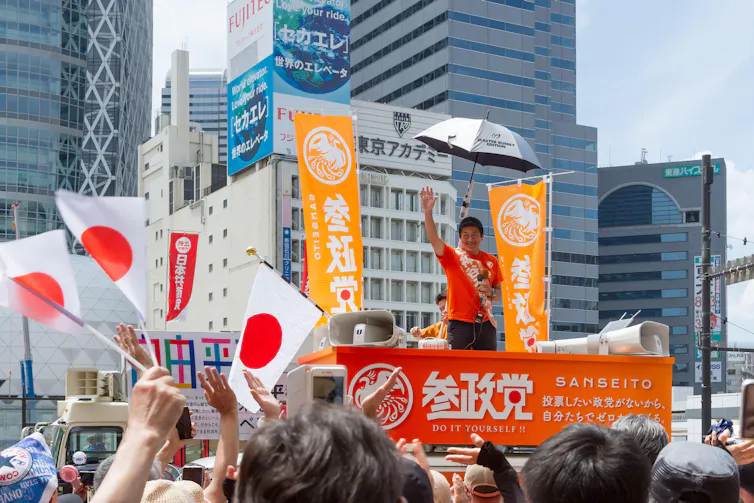 Kamiya greeting Sanseitō party supporters waving Japanese flags.