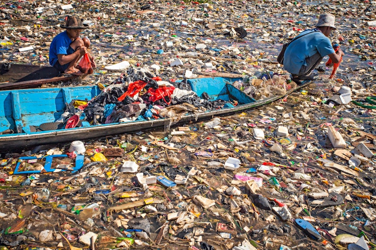 Two people ride a boat through heavily polluted water.