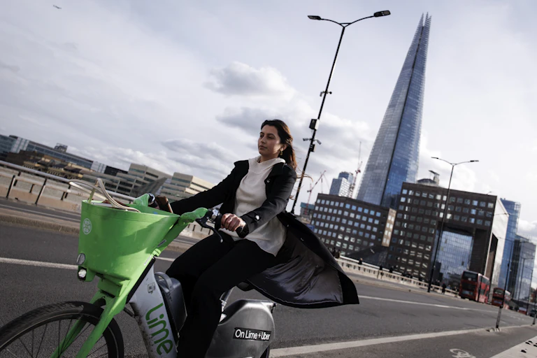 A woman on a green e-bike in London with the Shard in the background.