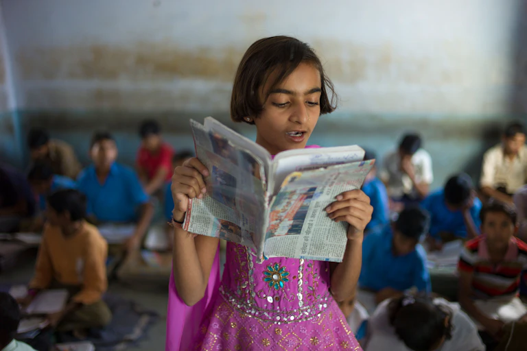 A young girl reads from an English textbook.