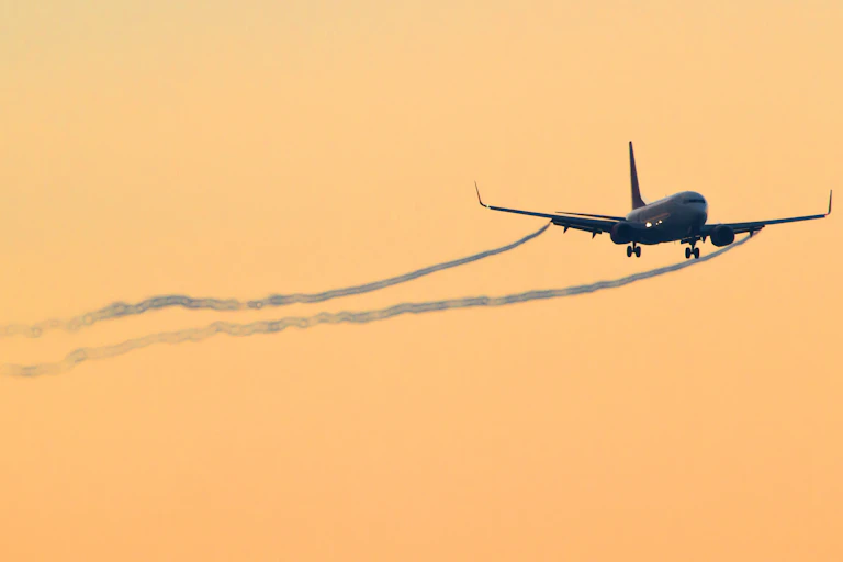 Un avion se prépare à atterrir sur un fond de ciel orangé au coucher du soleil.