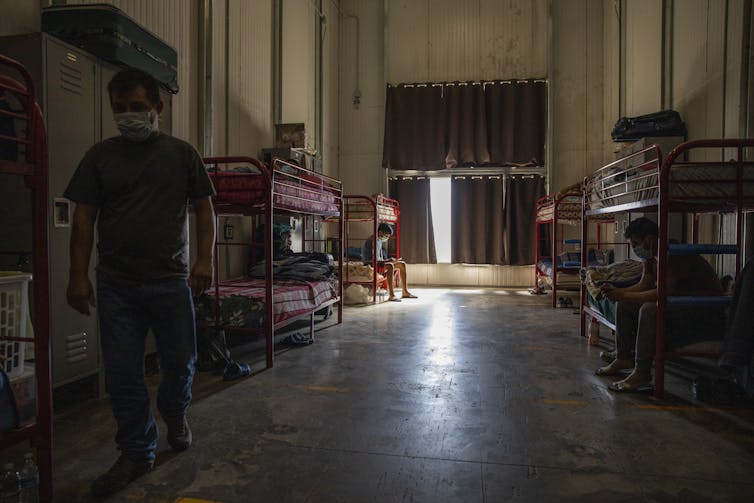 People wearing masks are seen in a dorm with bunk beds.