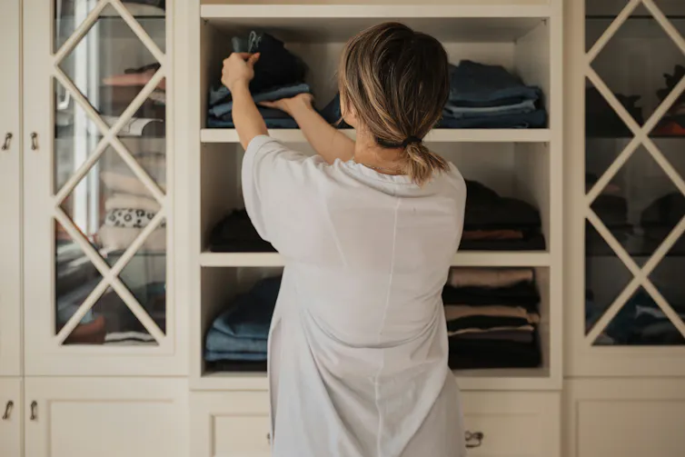 A woman, seen from behind, puts clothes away in a closet