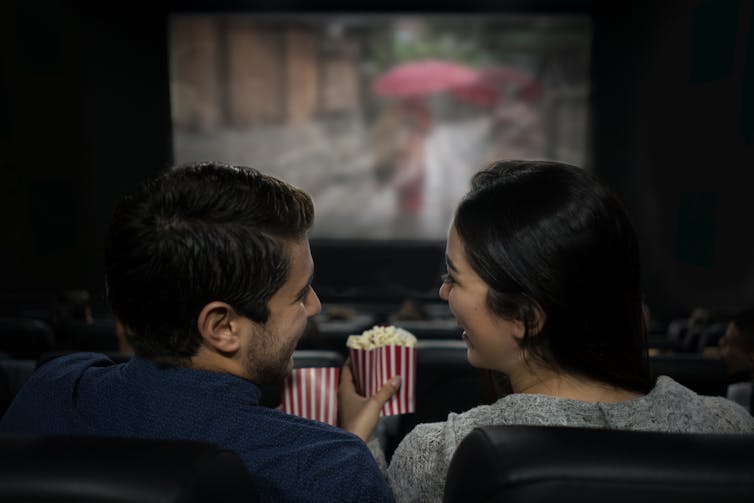 Dy njerëz duke ngrënë popcorn duke parë një film së bashku në kinema