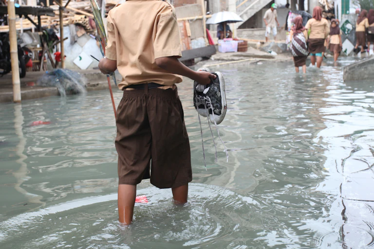 A person walking through a flood, holding their shoes