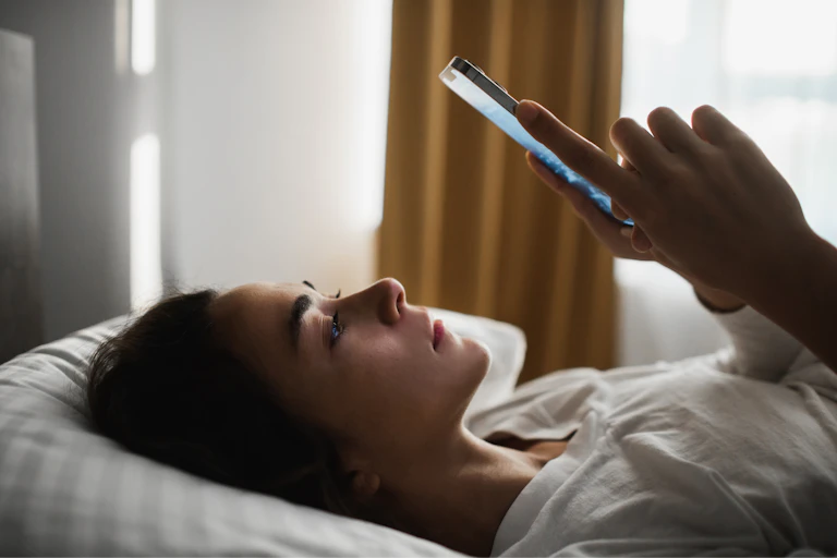 Woman looks at phone in bed