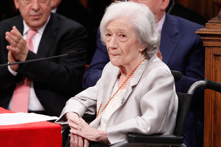 Una mujer mayor en silla de ruedas con pelo blanco se muerde los labios.