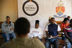A group of people sit around under a banner that says World Animal Protection