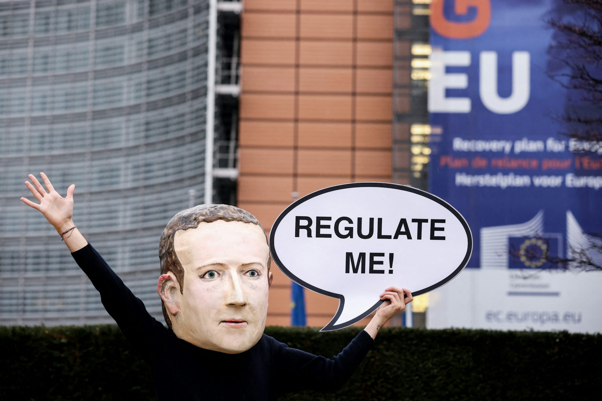 Un militant portant un masque à l'effigie du PDG de Facebook, Mark Zuckerberg, brandit une banderole sur laquelle on peut lire « Réglementez-moi » devant le bâtiment de la Commission européenne à Bruxelles. 