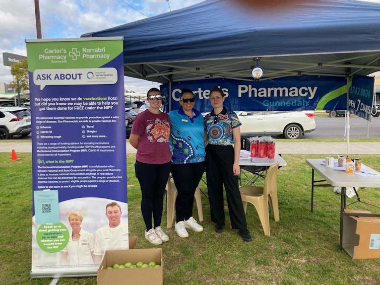 Three people stand under a marquee with a banner promoting safe medicine use.
