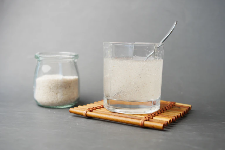 A glass jar containing soluble fibre and a glass of water with a spoon of fibre dissolving in it.