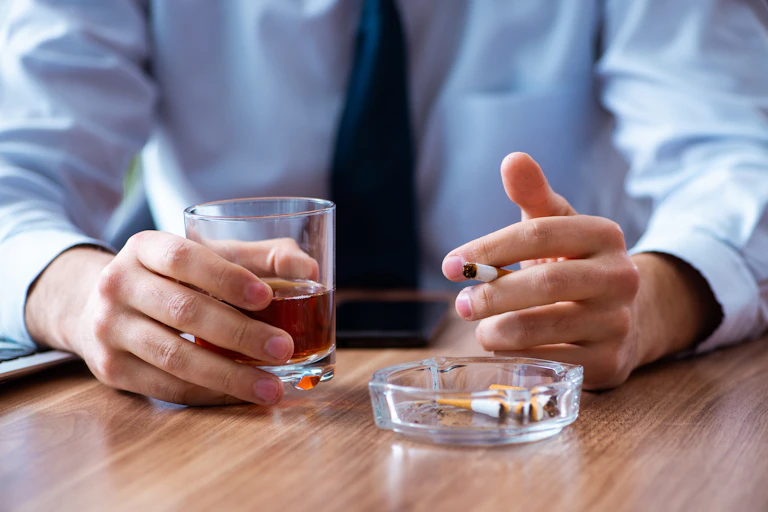 Un employé fume des cigarettes et tient une verre d'alcool à la main.