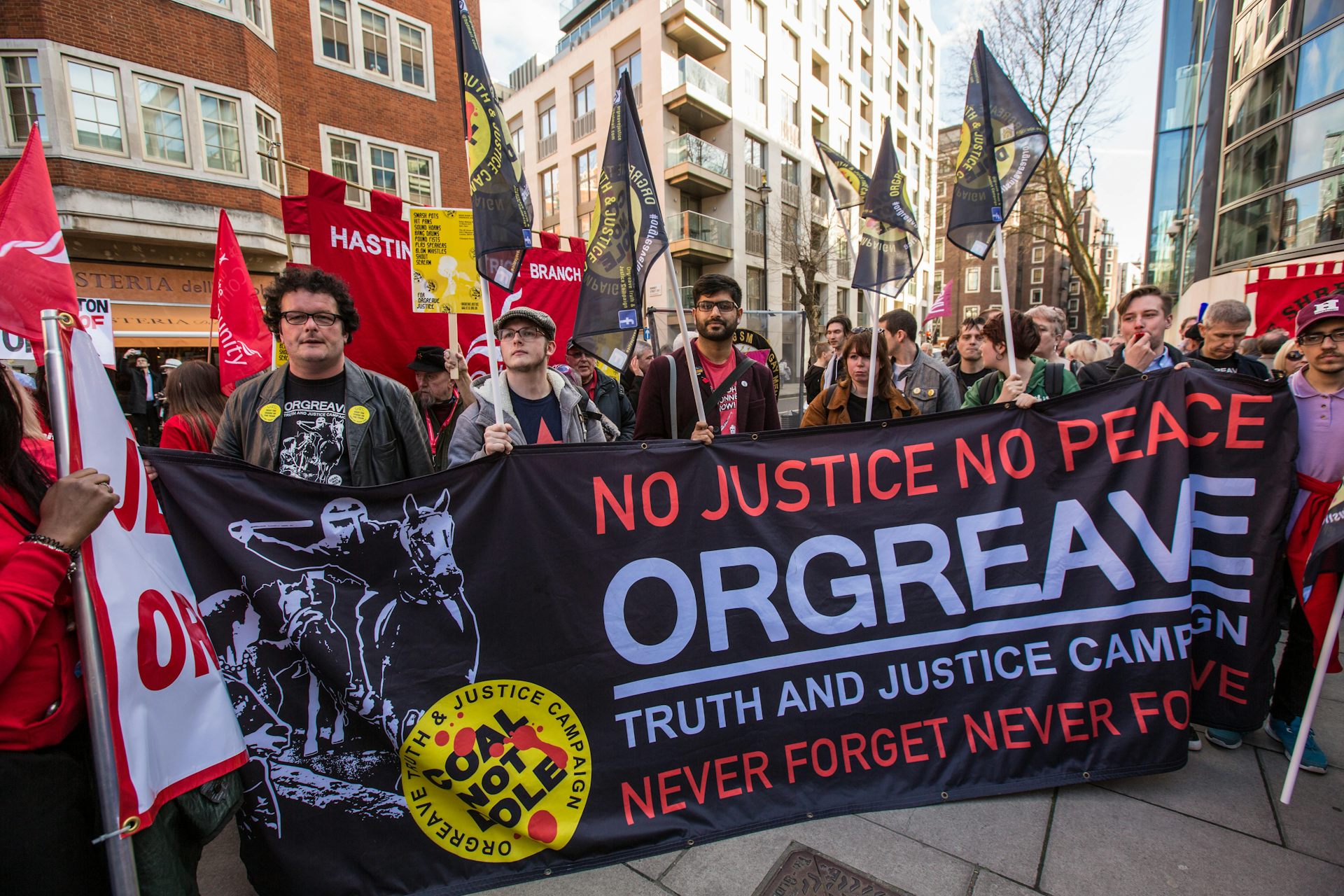Protesters holding a black, white and red banner reading 'no justice, no peace, orgreave truth and justice campaign'