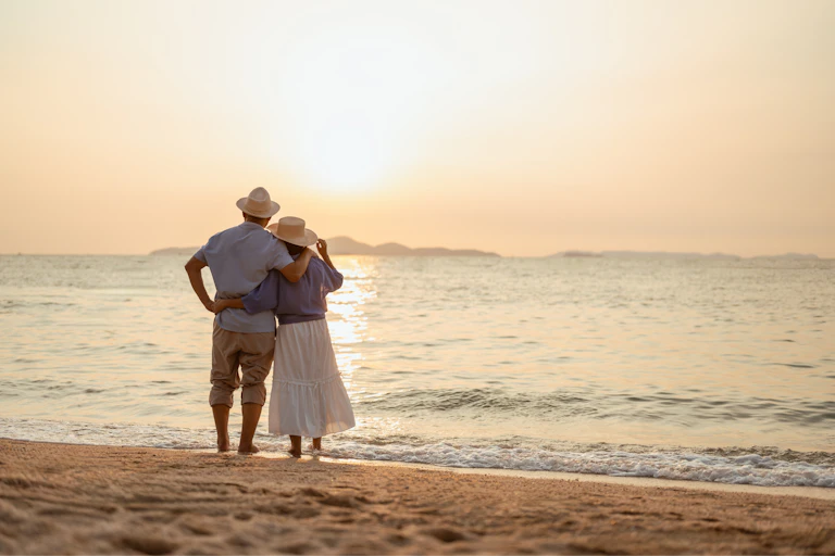 Couple on sandy shore watching sunset.