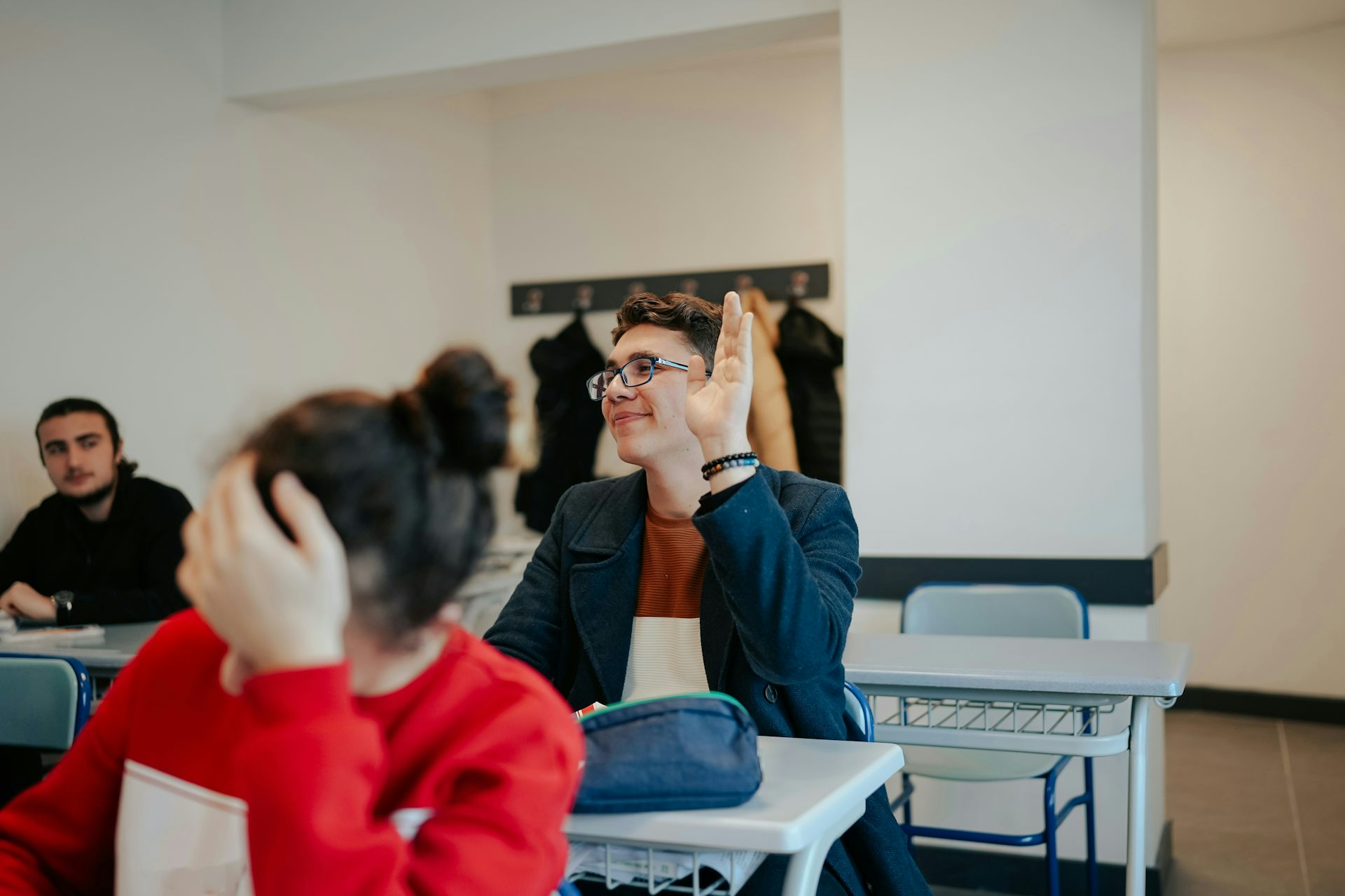 A person with raised hand in a classroom.