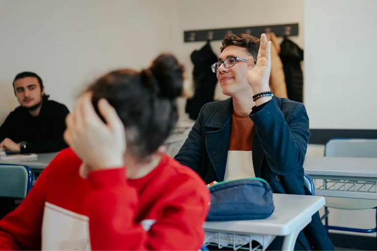 A person with raised hand in a classroom.