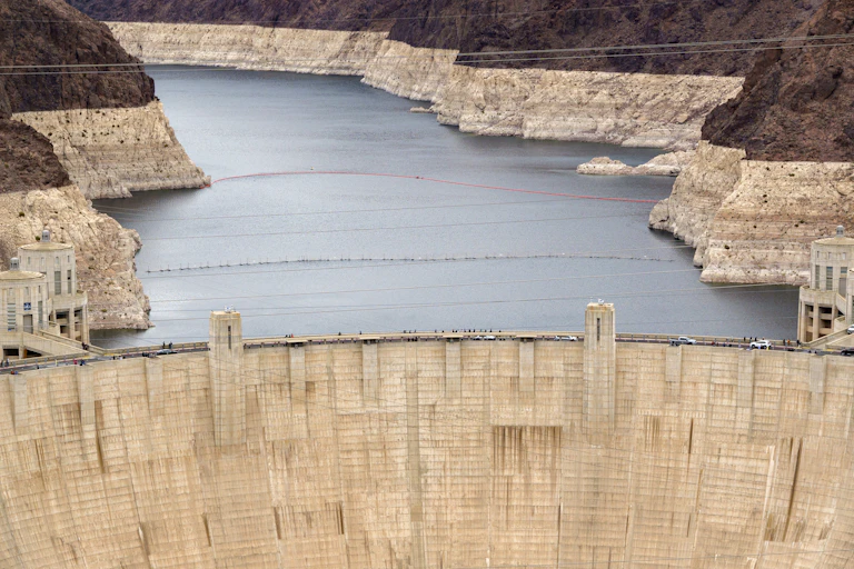A large concrete wall holds back a body of water, with exposed rock visible around its edges on slopes that lead up to vegetation.