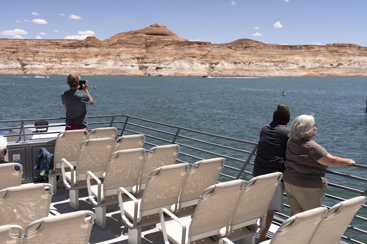 People stand on a boat looking at a body of water and mountains beyond.