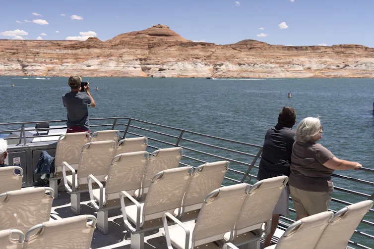 People stand on a boat looking at a body of water and mountains beyond.