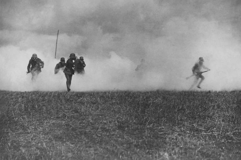 A vintage photo of soldiers wearing gas masks running through a cloud of smoke.