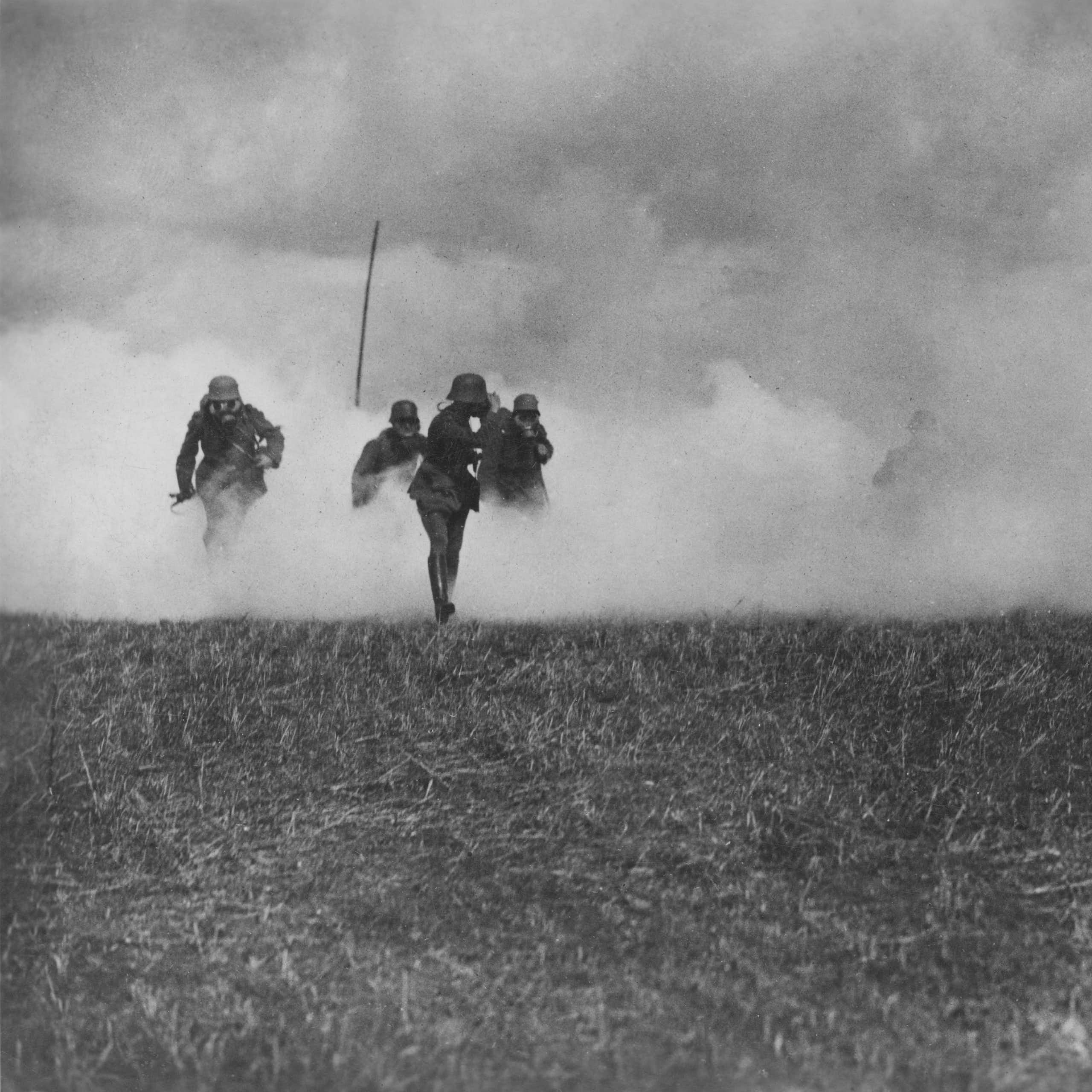 A vintage photo of soldiers wearing gas masks running through a cloud of smoke.