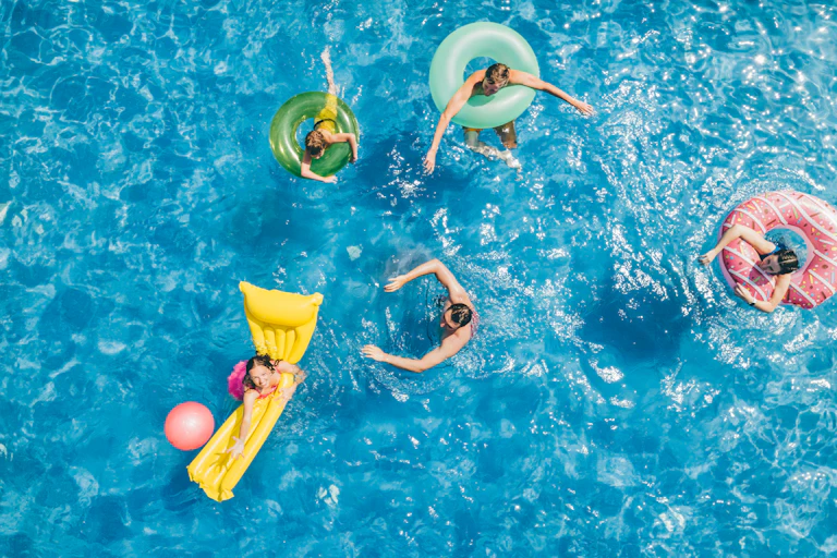 Aerial shot of several people on rafts and pool donuts in clear blue pool water