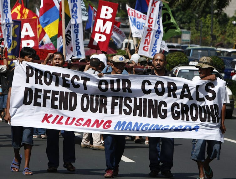 people protesting carrying a sign reading protect our corals, defend our fishing grounds