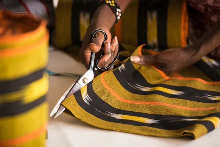 Une main tenant des ciseaux, coupant un tissu rayé.
