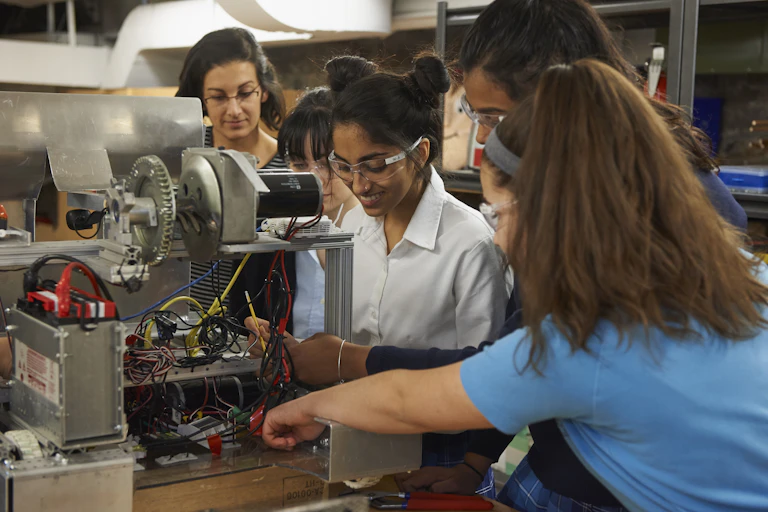 A group of women in an engineering lab, standing around a piece of machinery.