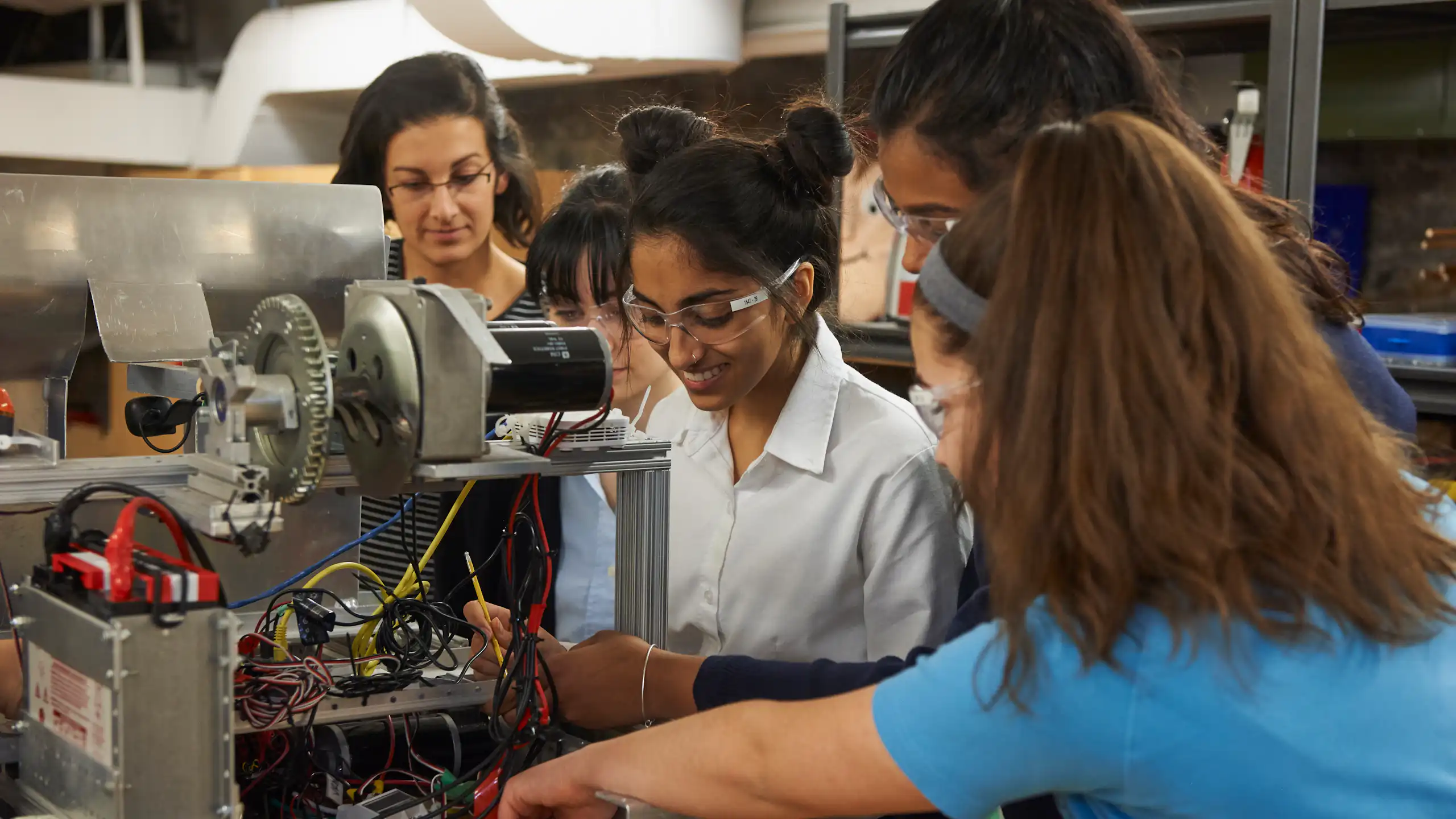 A group of women in an engineering lab, standing around a piece of machinery.