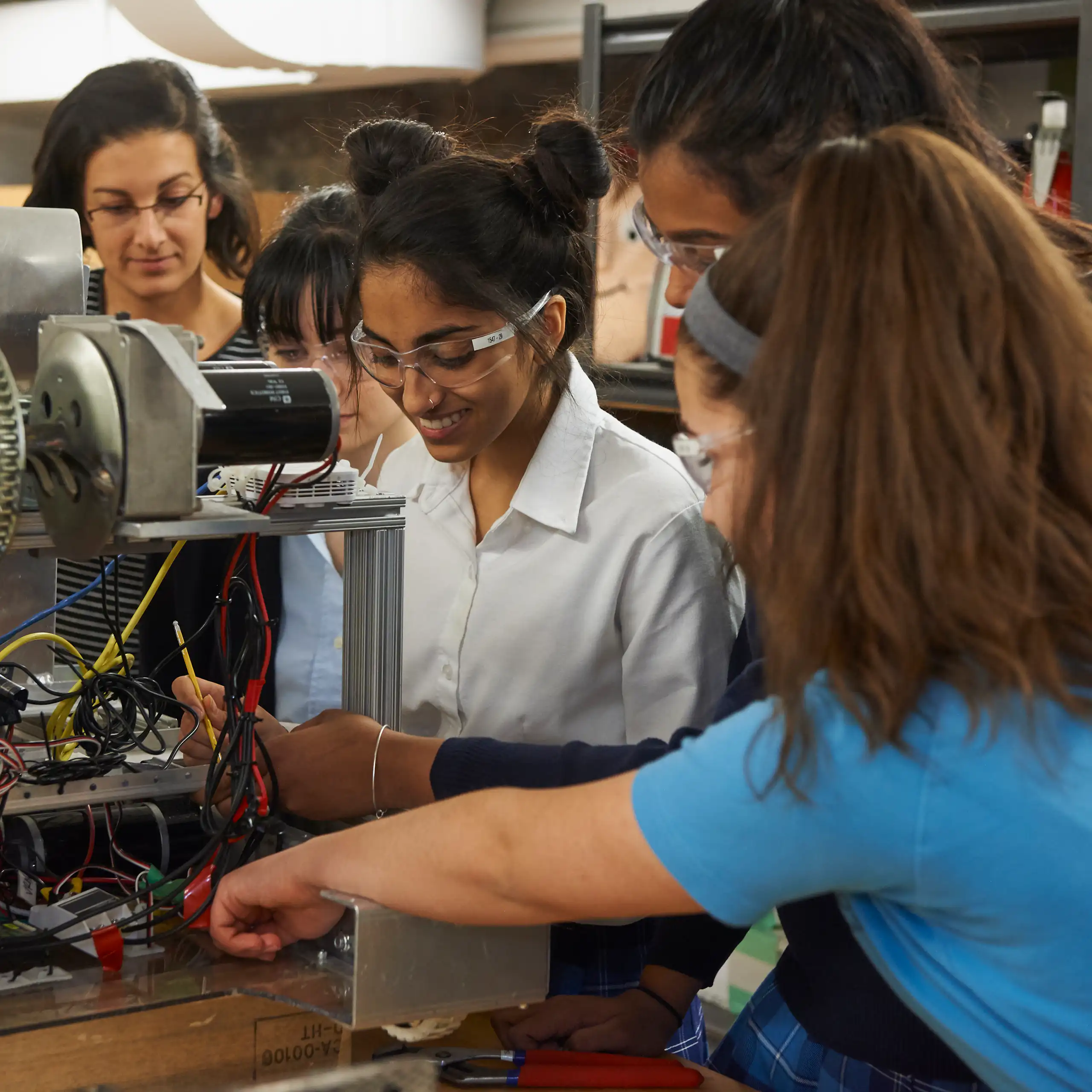 A group of women in an engineering lab, standing around a piece of machinery.
