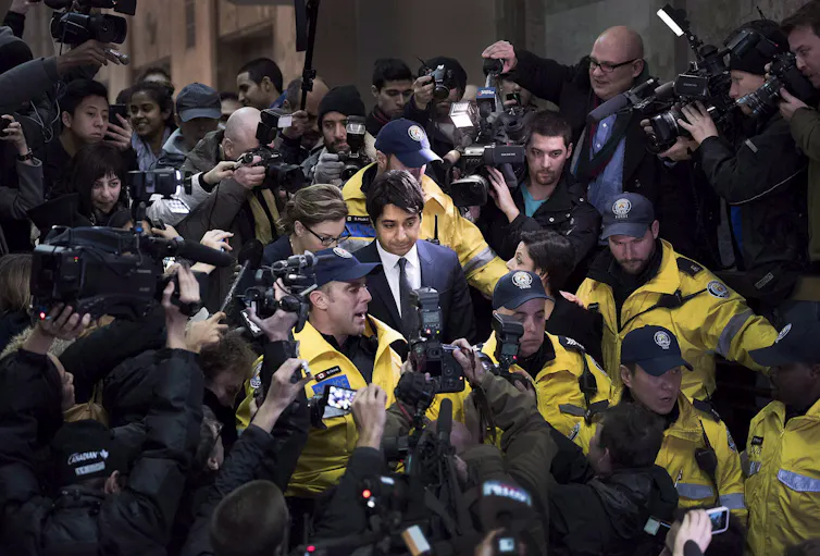 A man with dark hair is surrounded by police as he walks through a crowd.