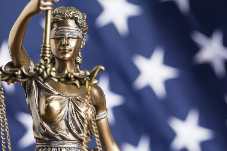 A statue of Justice, blindfolded, set against the blue background and white stars of the American flag.
