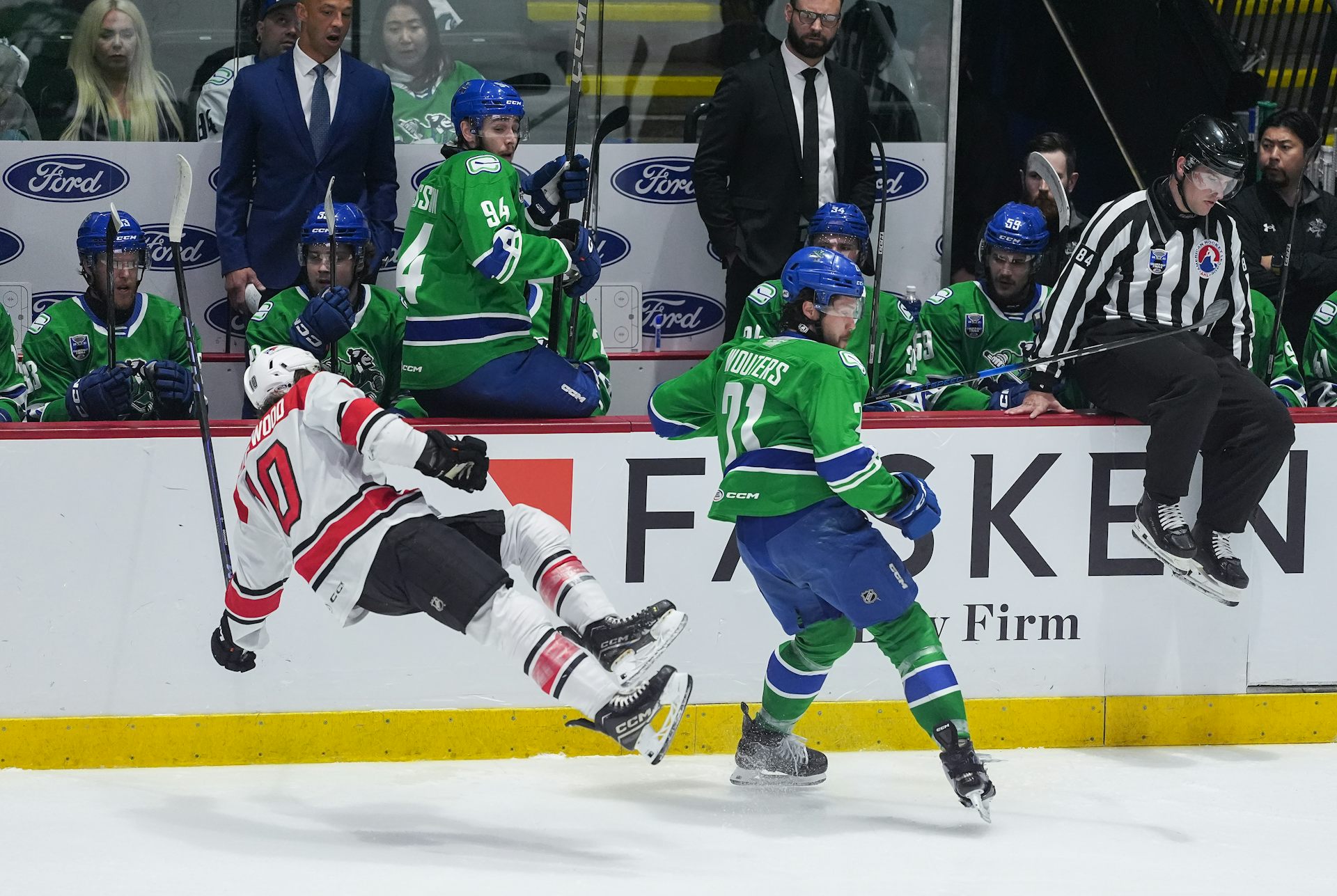 El jugador de hockey cae al lado del jugador del oponente como juez en los tableros durante el juego de hockey.