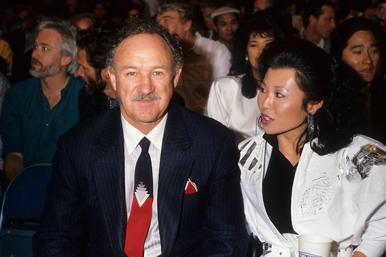 An older man in a tie and with a mustache sits with a younger woman with lustrous black hair.