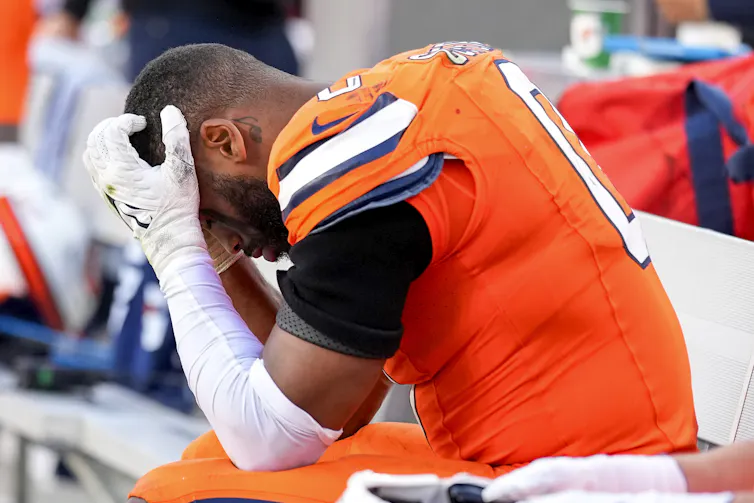 A football player in an orange jersey with his face in his hands.