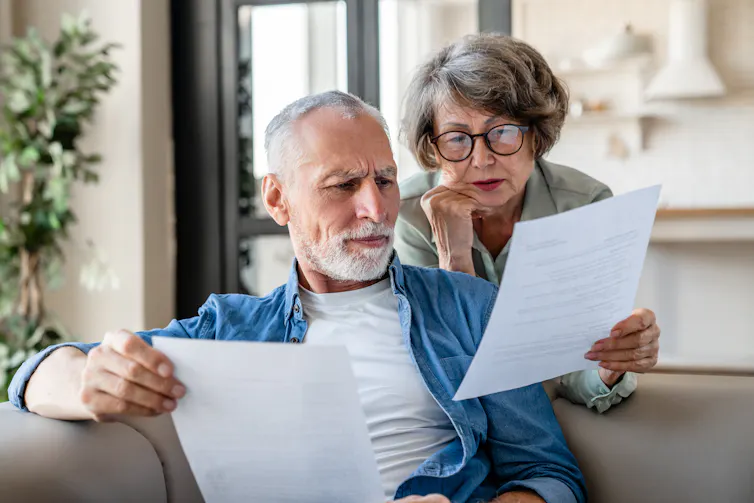 An older man and an older woman look puzzled while reading a document.