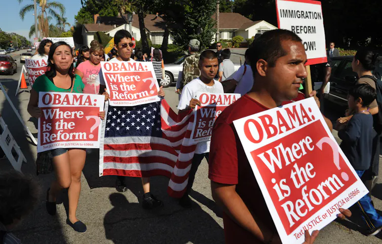 Several people holding signs and an American flag walk in a protest march.