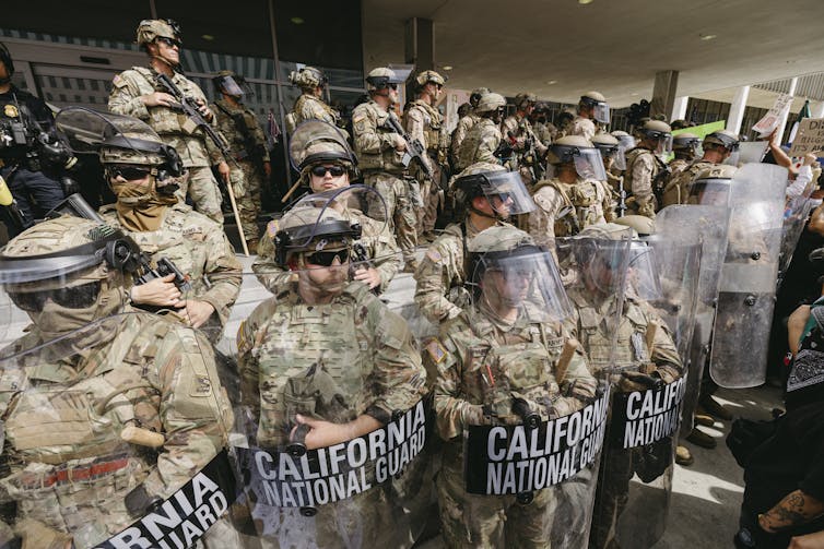 Several men in military gear stand watch on the steps of a building.