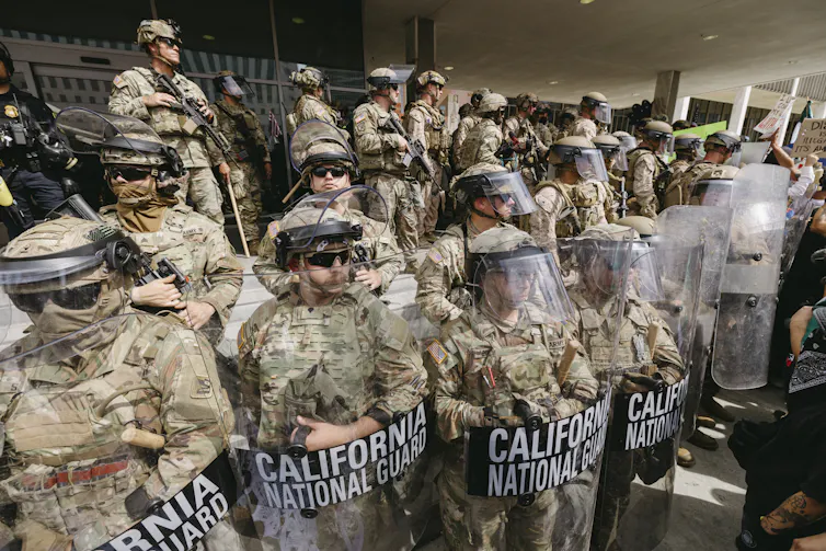 Several men in military gear stand watch on the steps of a building.