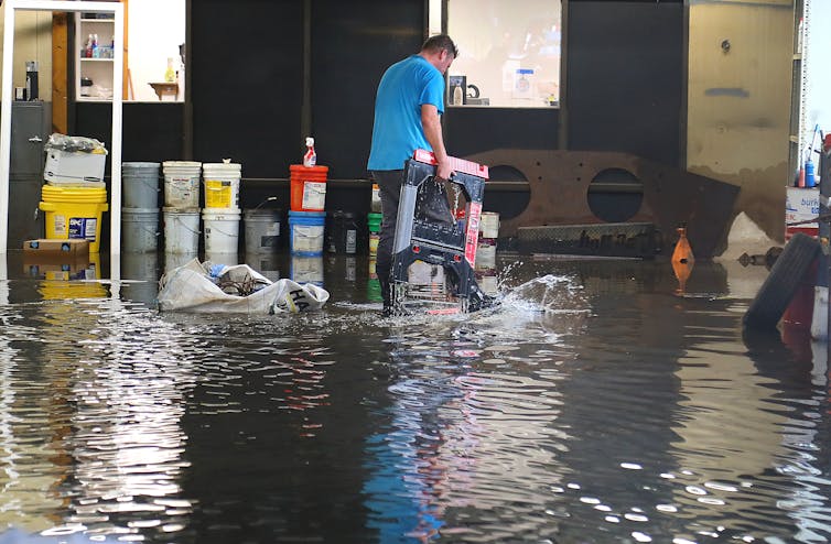 A man standing in ankle-deep water moves equipment to safety in a construction business.