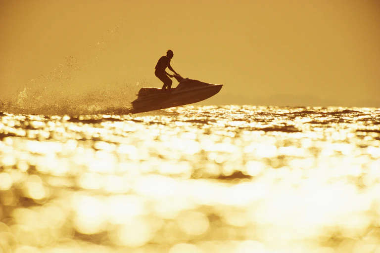 Person riding jet ski at sunset, light shimmering on water