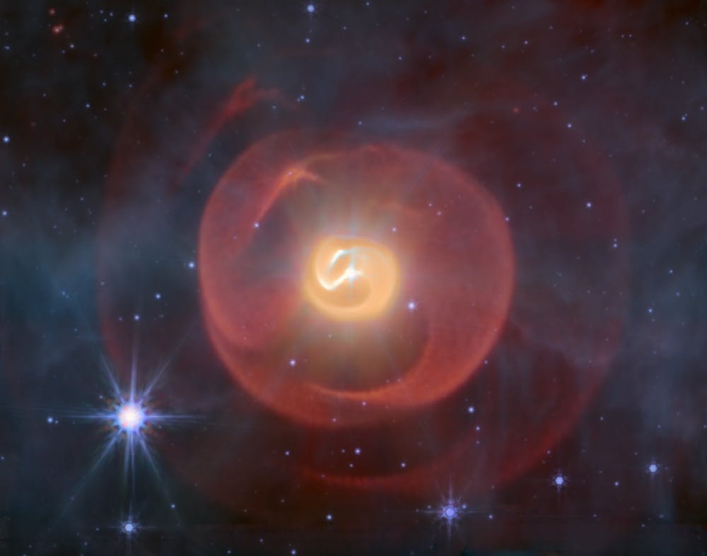 Three shells of dust, resembling coiled snakes, the middle one yellow and the outer ones red against a background of blue stars.