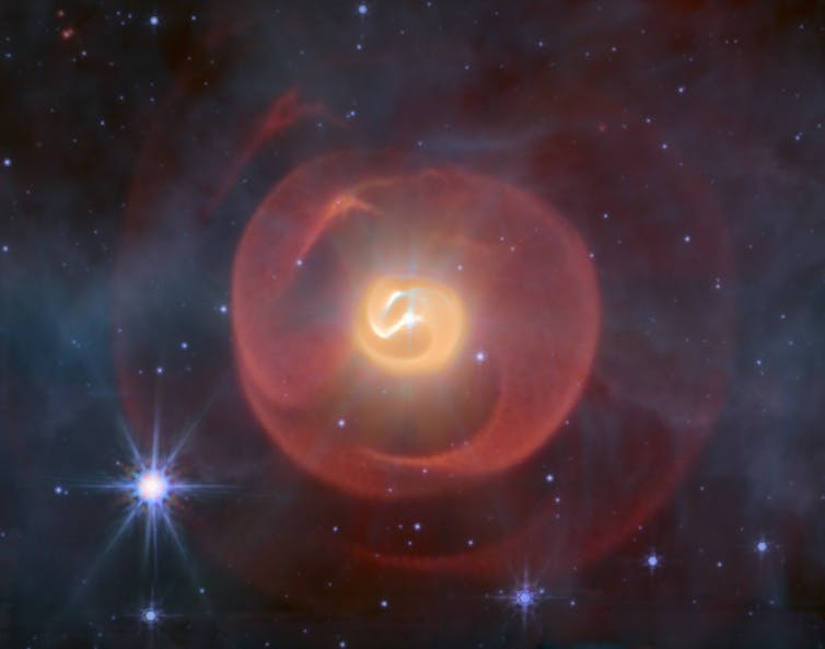 Three shells of dust, looking like coiled snakes, the middle one yellow and the outer ones red against a background of blue stars.