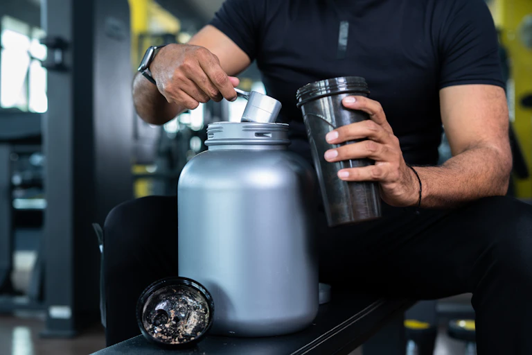 A man scoops protein powder into a shaker bottle.