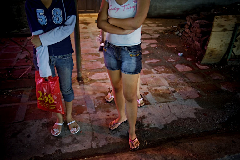 The lower half of three young women is shown in a red light district in Asia.