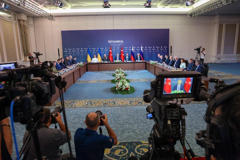 Negotiators from Russia and Ukraine as well as representatives of the Turkish government sit along a three-sided table facing press photographers.