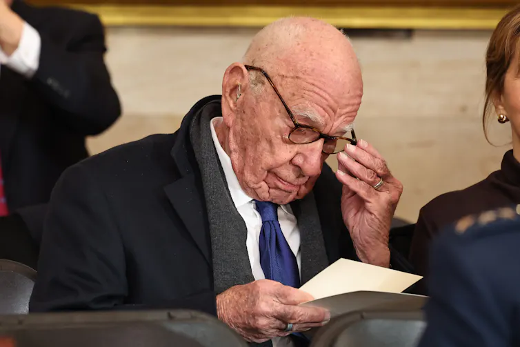 Murdoch adjusts his glasses while reading a programme at the inauguration