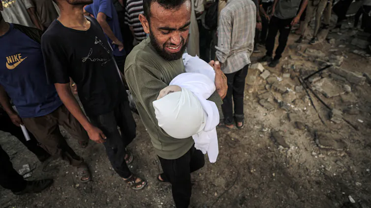 A Palestinian man cries as he holds the body of a baby after an Isaeli airstrike in Gaza.