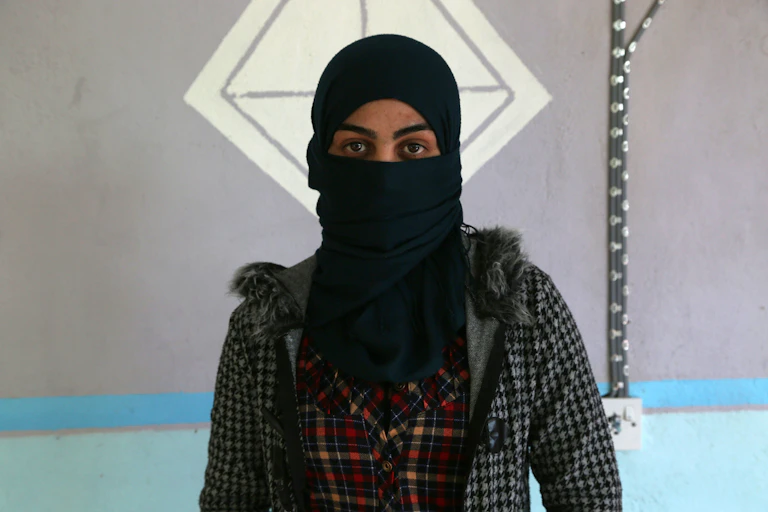 A Yazidi woman stands with her face partially covered.